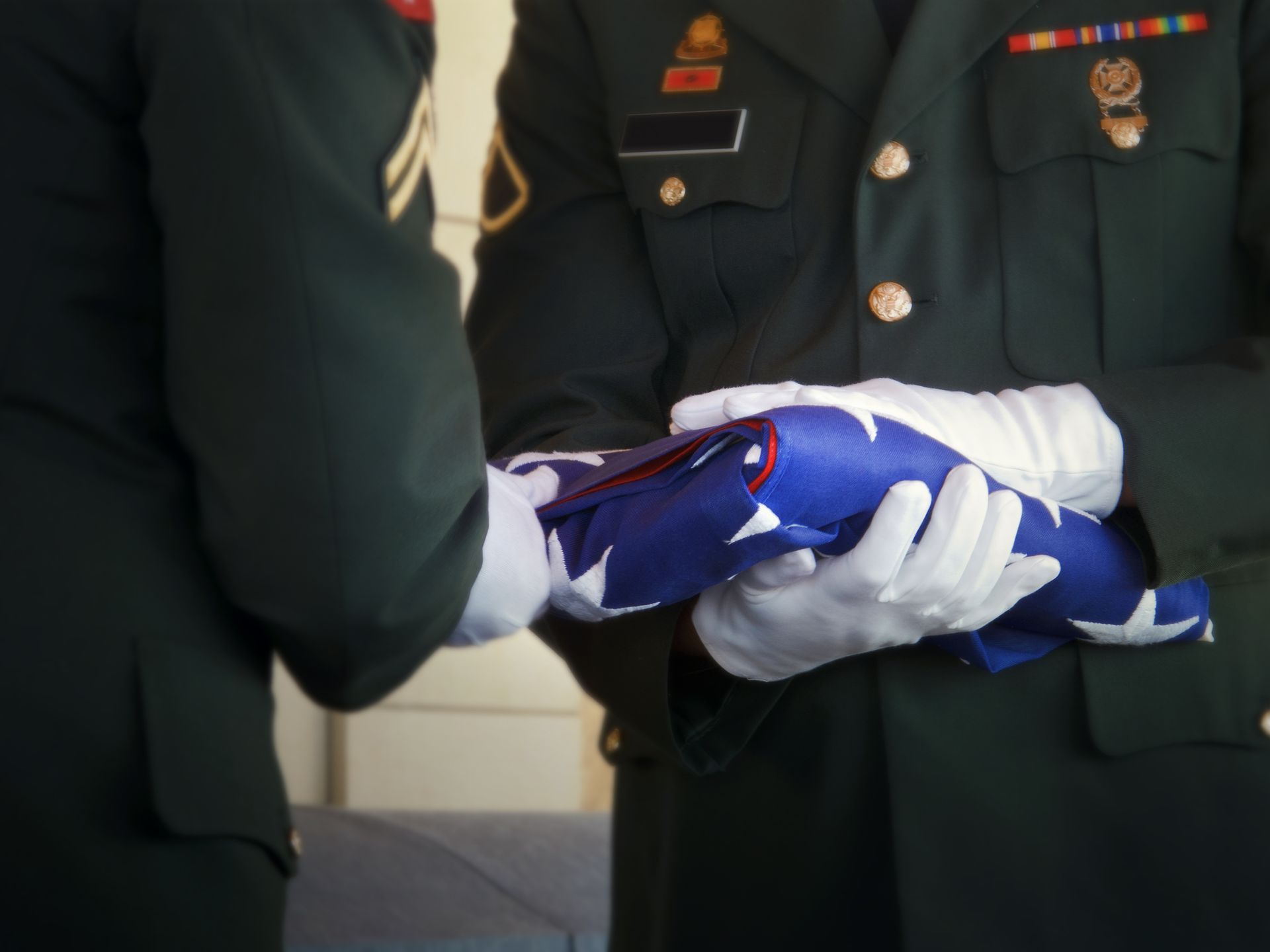 Soldiers folding an American flag, wearing white gloves and dark green uniforms.