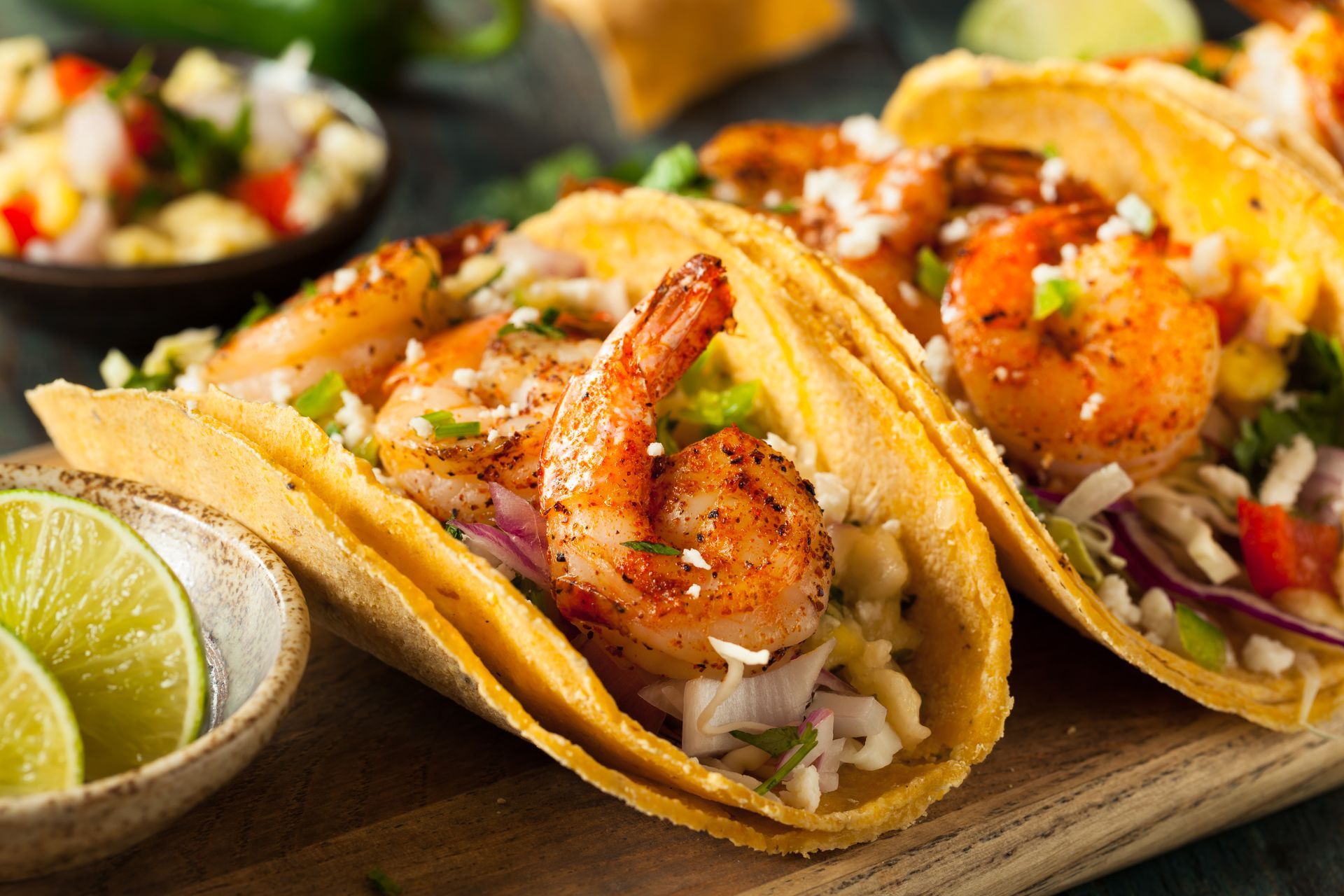 Shrimp tacos with visible shrimp, cabbage, and red onion, served with lime wedges and salsa.