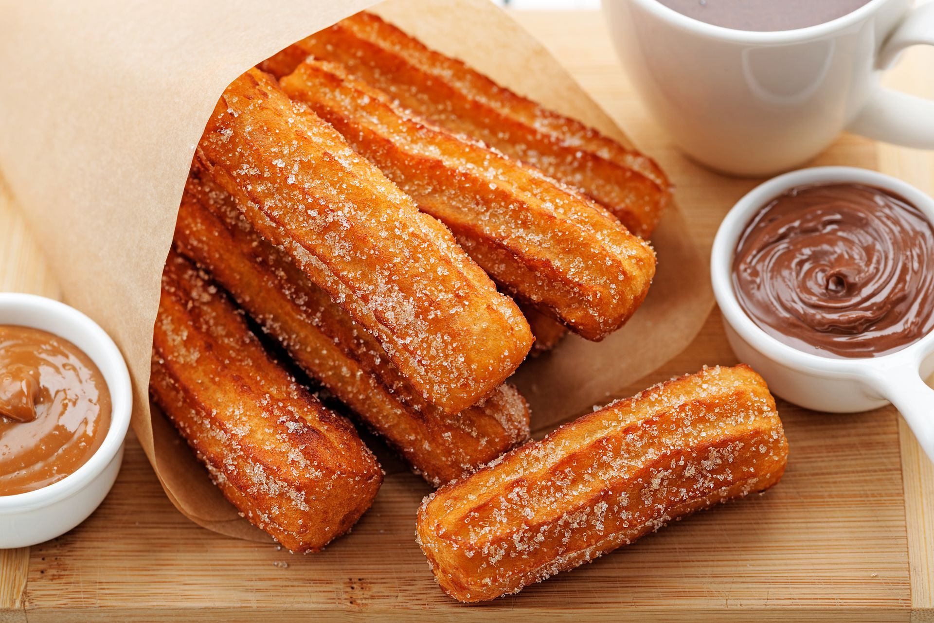Golden churros dusted with sugar, served with chocolate and caramel dips, and a cup of hot chocolate. Golden churros dusted with sugar, served with chocolate and caramel dips, and a cup of hot chocolate.