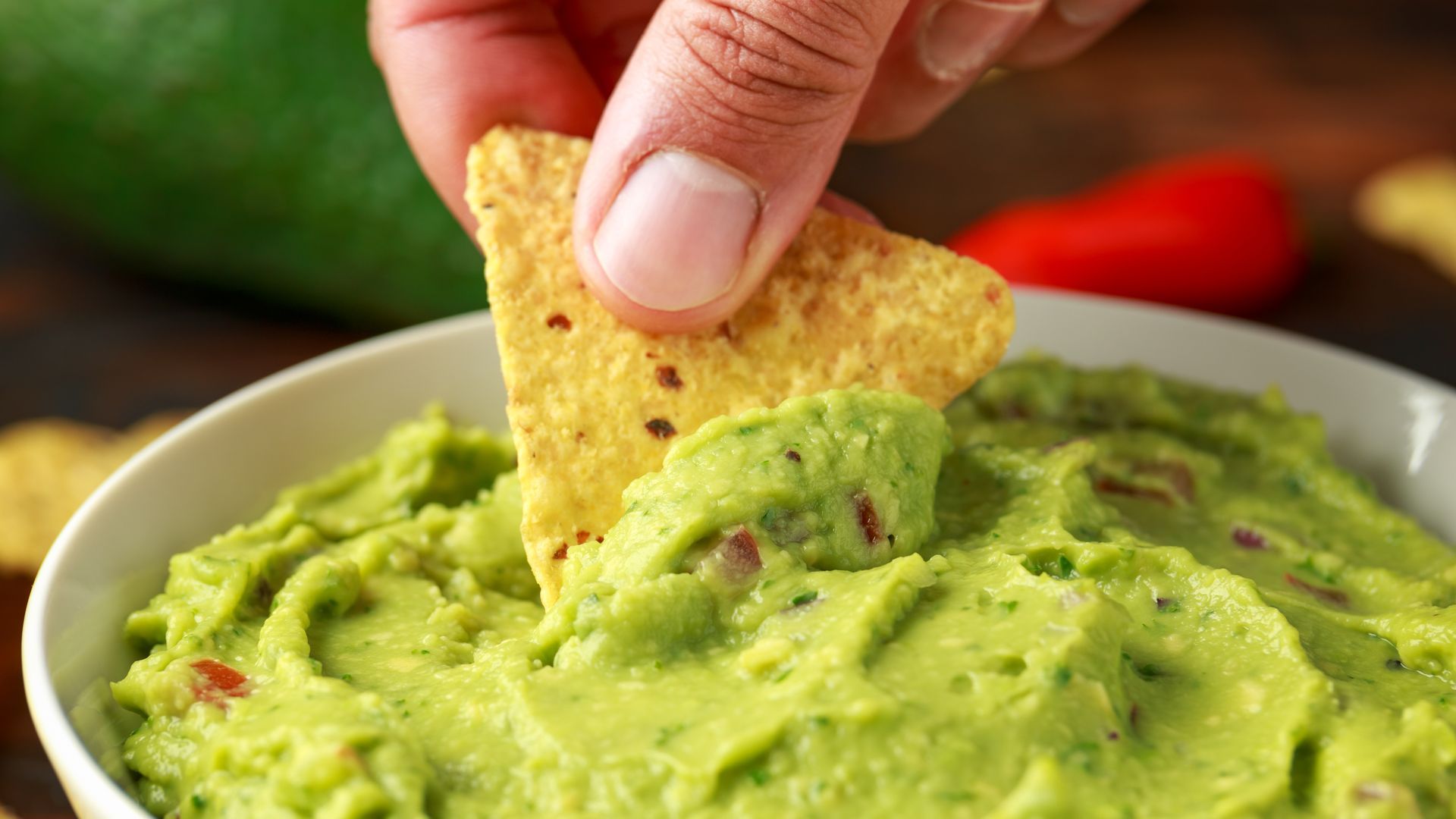 Hand dipping a tortilla chip into creamy green guacamole.