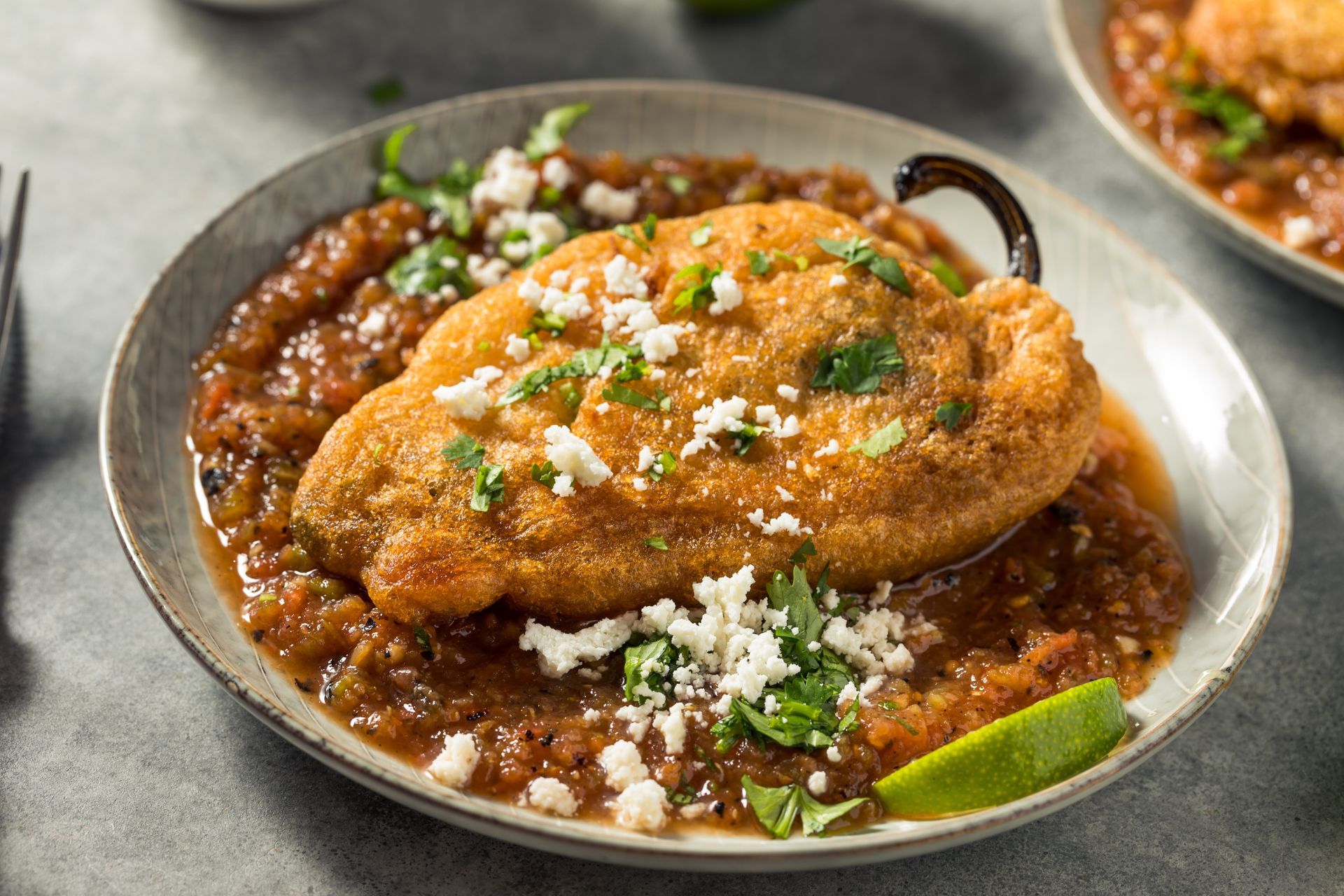 Chile relleno with salsa, garnished with cheese, cilantro, and lime on a plate.