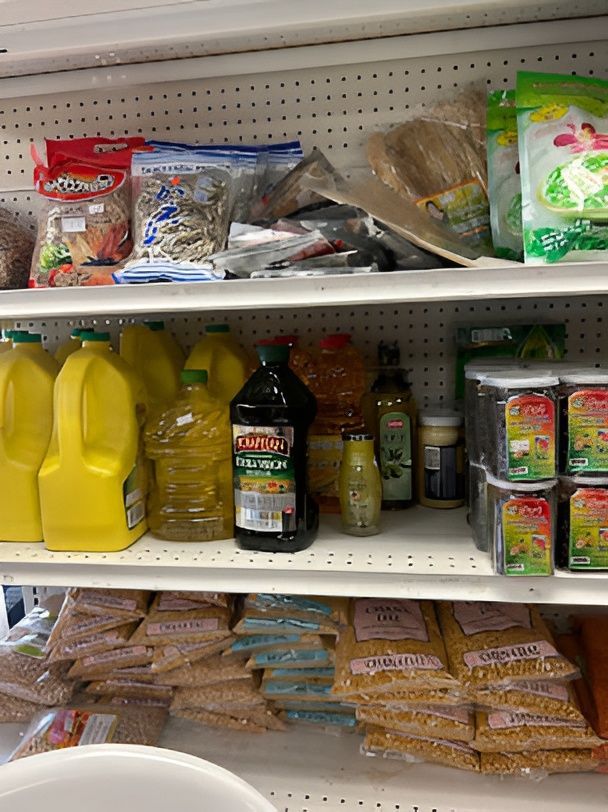 Shelves of various food items: oil jugs, packaged grains, and other groceries in a store setting.