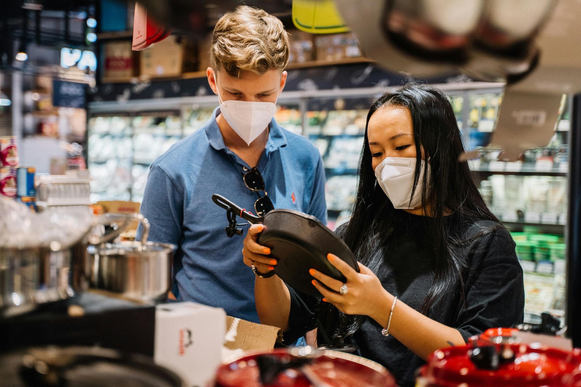 Couple wearing masks examining cookware in a store.