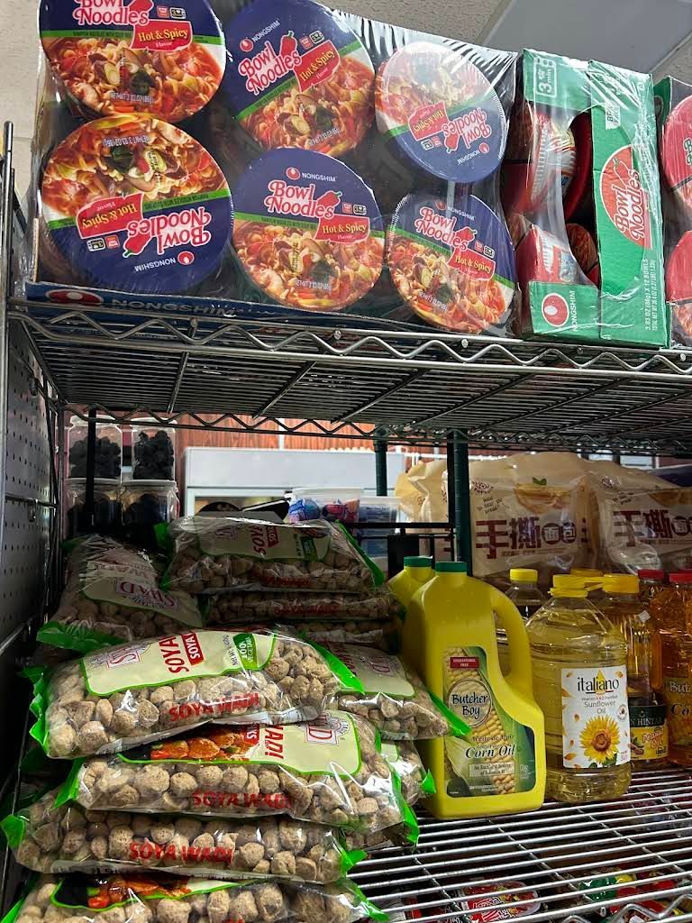 Shelves stocked with packaged food items including noodles, snacks, cooking oil, and fruits in a grocery store.