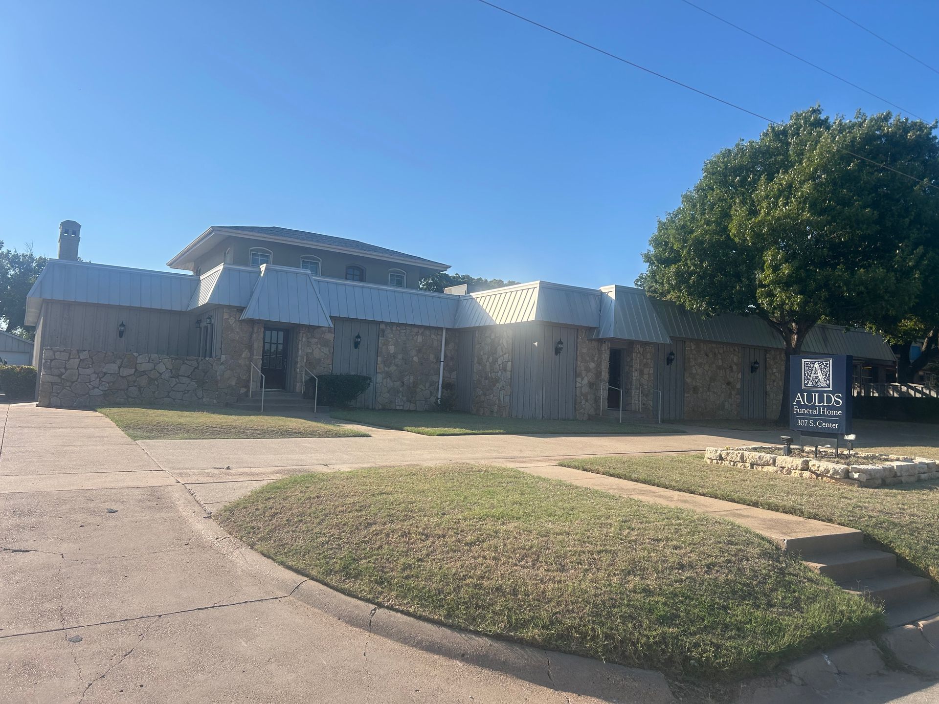 White building with a brick sidewalk and a tree in front, under a blue sky.