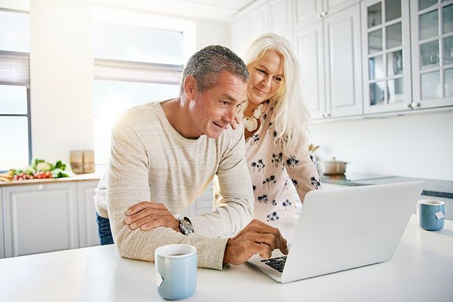 Older couple in kitchen looking at a laptop together, smiling.