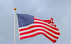 American flag waving in the wind, red and white stripes, blue field with white stars, against a cloudy sky.