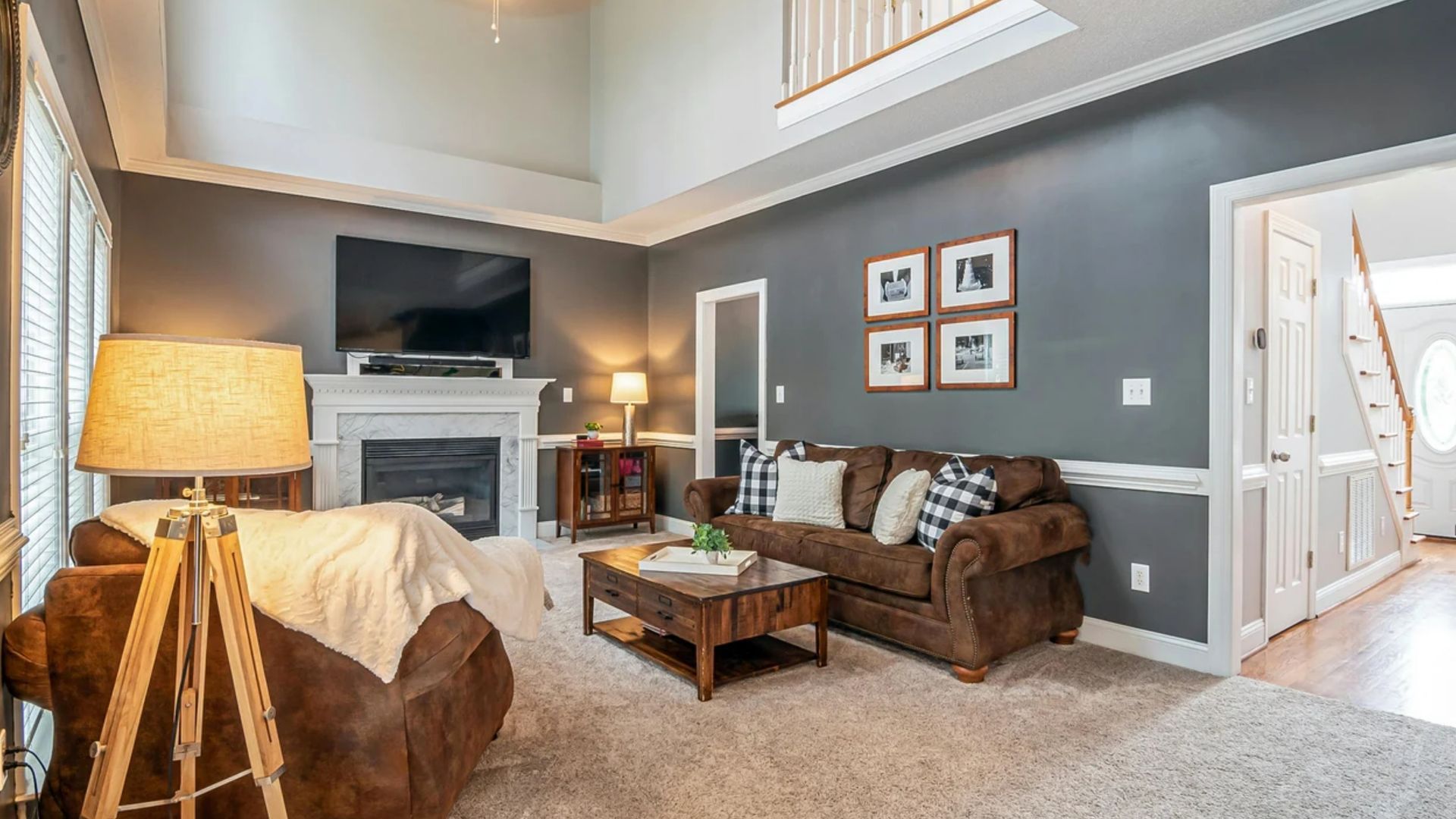 Modern living room with gray walls, brown sofas, fireplace, TV, and warm floor lamp lighting