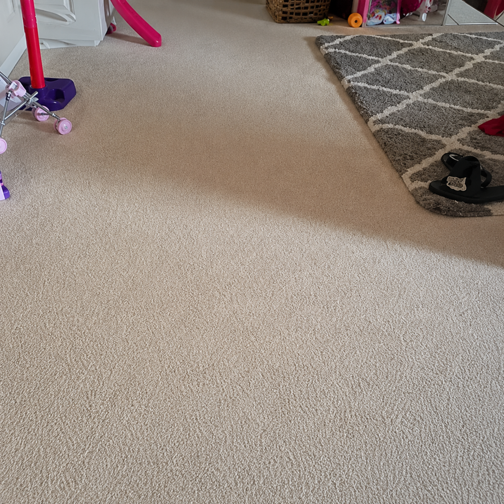 Carpeted living room with a gray rug, kids’ toys, and a pair of shoes near the edge.