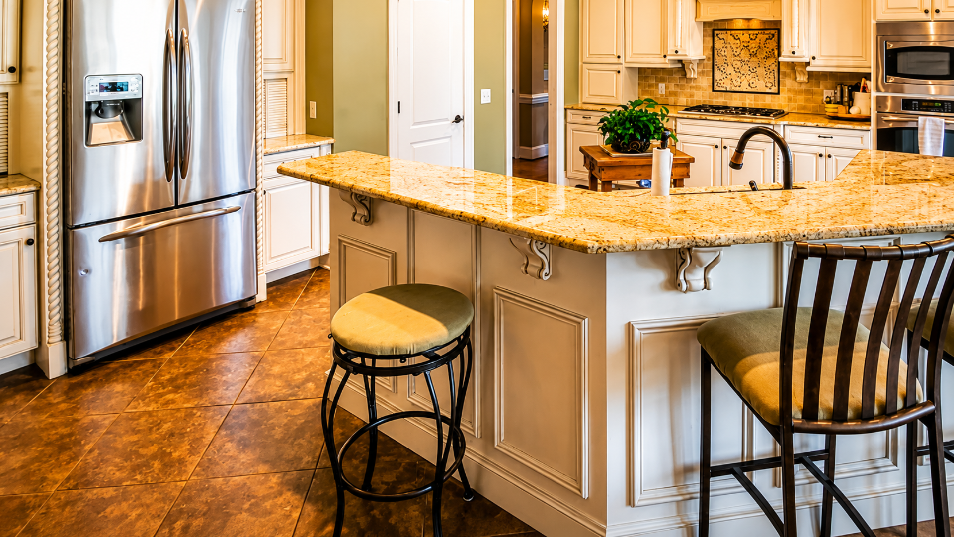 Bright kitchen with stainless steel fridge, granite island, and two stools by a tiled floor