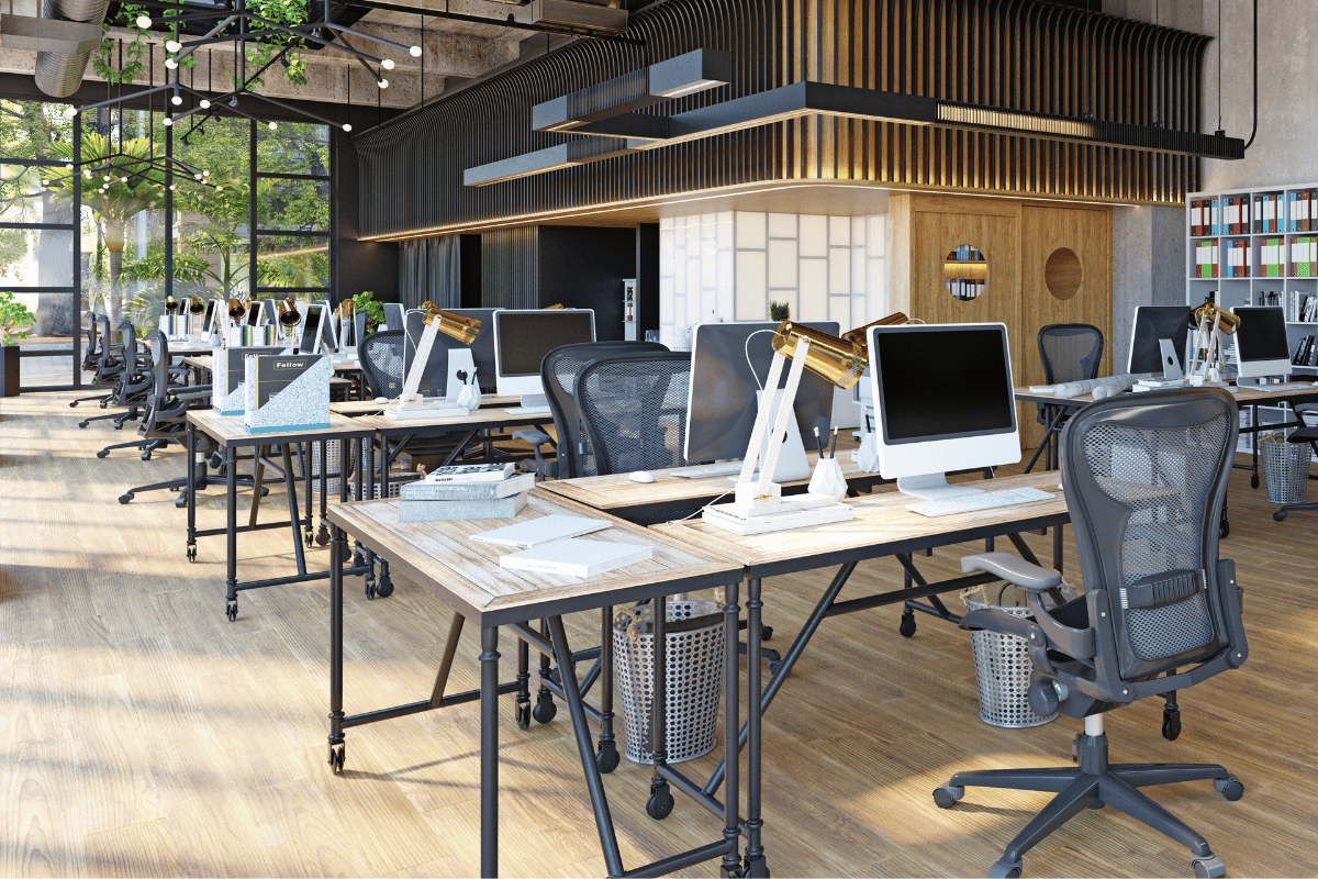 An open-plan office with desks, computers, and chairs. Natural light streams in, highlighting the wood floors and modern design.