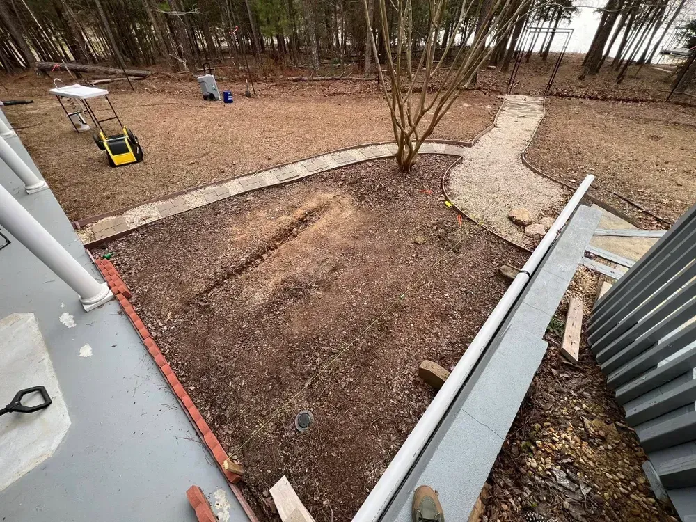 Backyard with leaf-covered ground, curved stepping-stone paths, and a bamboo grove beyond a fenced patio.