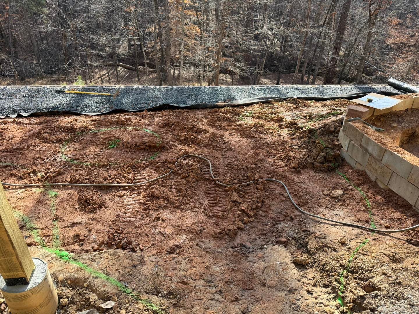 Backyard excavation area with bare soil, mesh-covered slope, and stacked retaining wall blocks