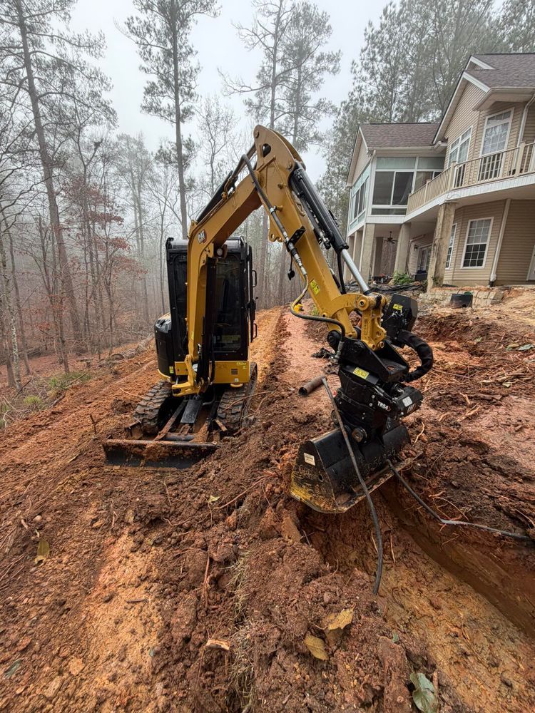 Excavator clearing a muddy hillside beside a house in a wooded area on a foggy day