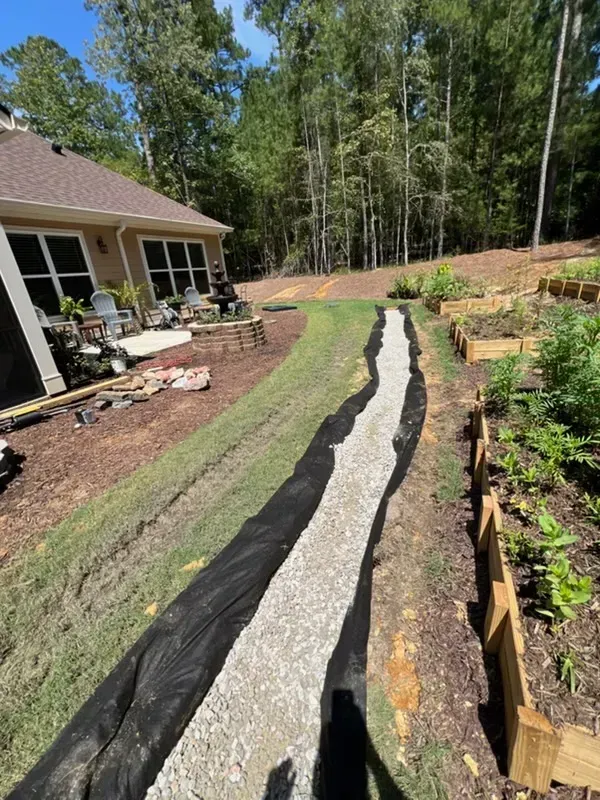 Landscaped backyard with a narrow gravel drainage trench beside a house and garden beds