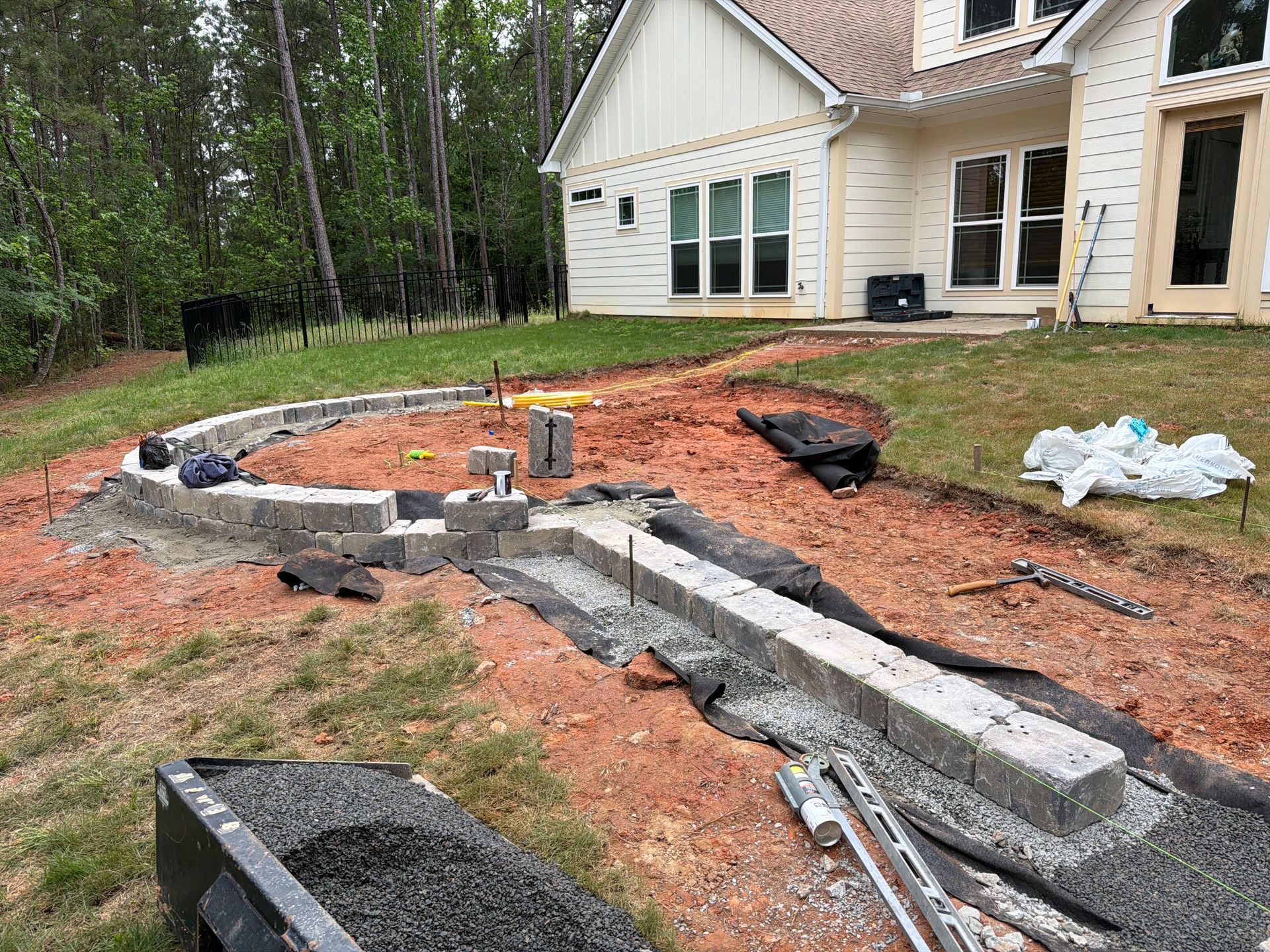 Backyard construction with curved stone retaining wall, dirt excavation, and a house in the background
