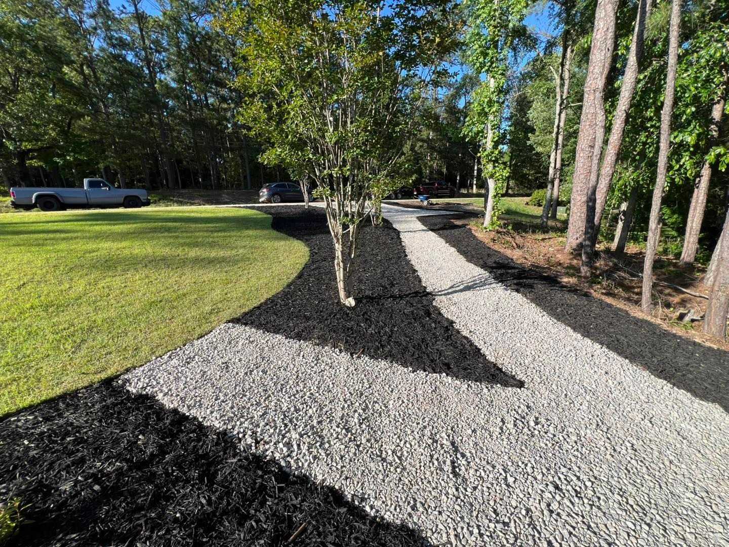 Gravel landscape path curving through a grassy yard with trees and parked cars in the background