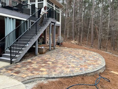 Stone patio beside a raised deck and stairs, with a wooded backyard beyond.