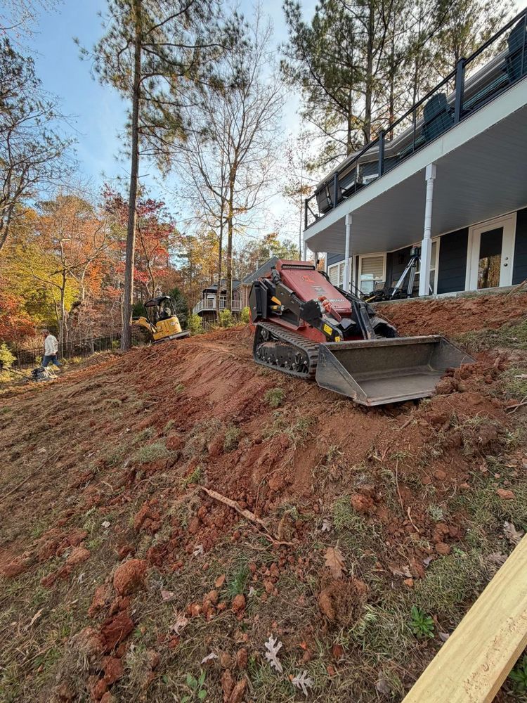 Bulldozer on a sloped dirt lot beside a building, clearing soil near trees in fall.