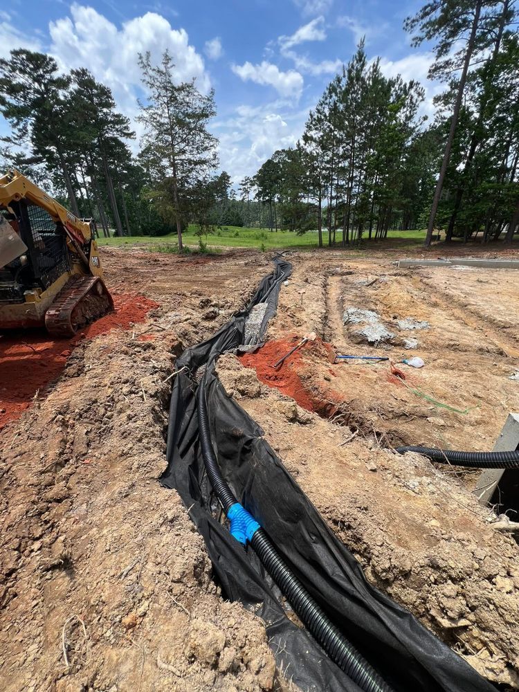 Construction site with excavator, trench, and black erosion-control fabric on muddy ground.