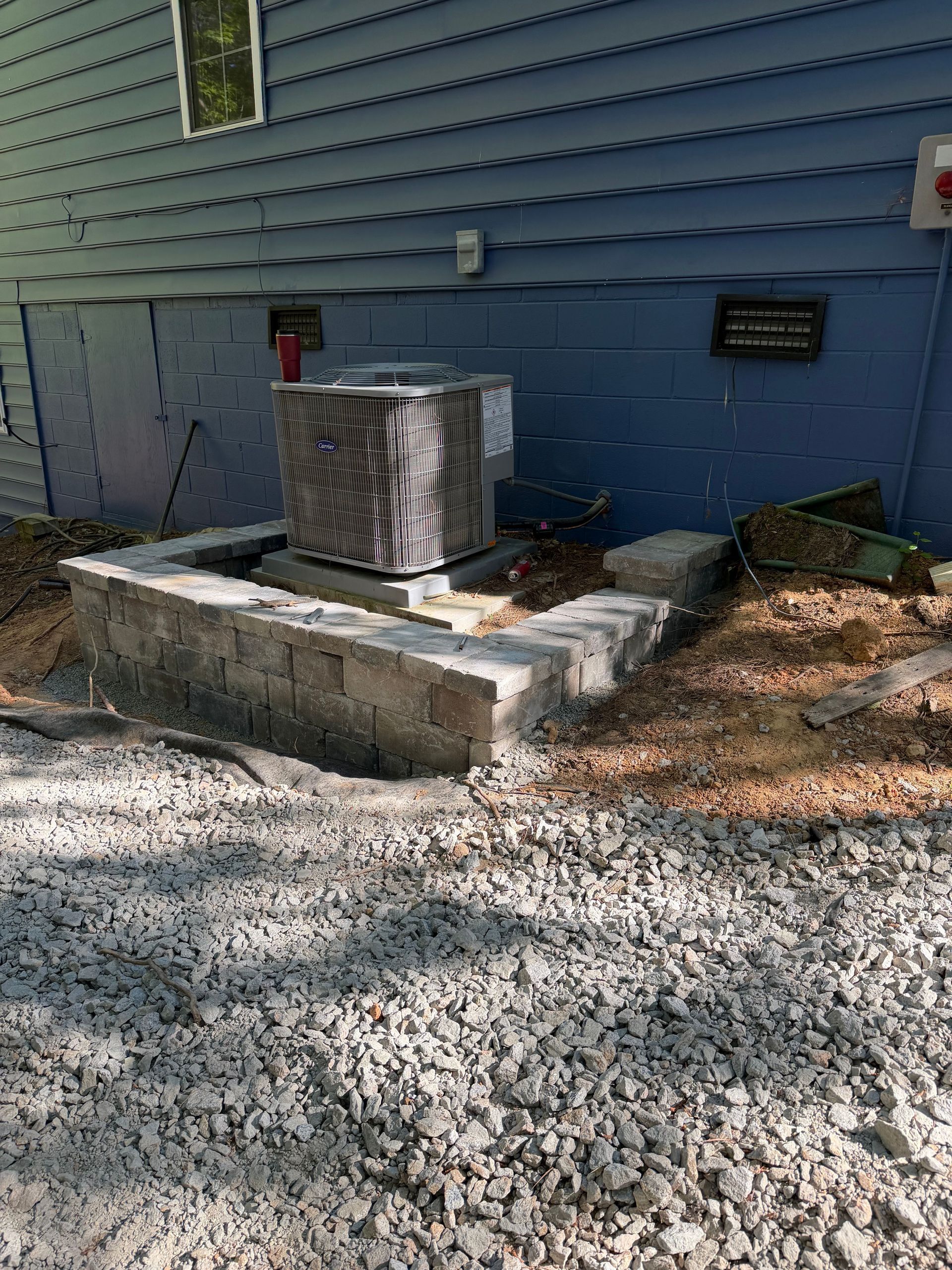 Outdoor HVAC unit on a concrete pad beside a blue house with gravel ground around it