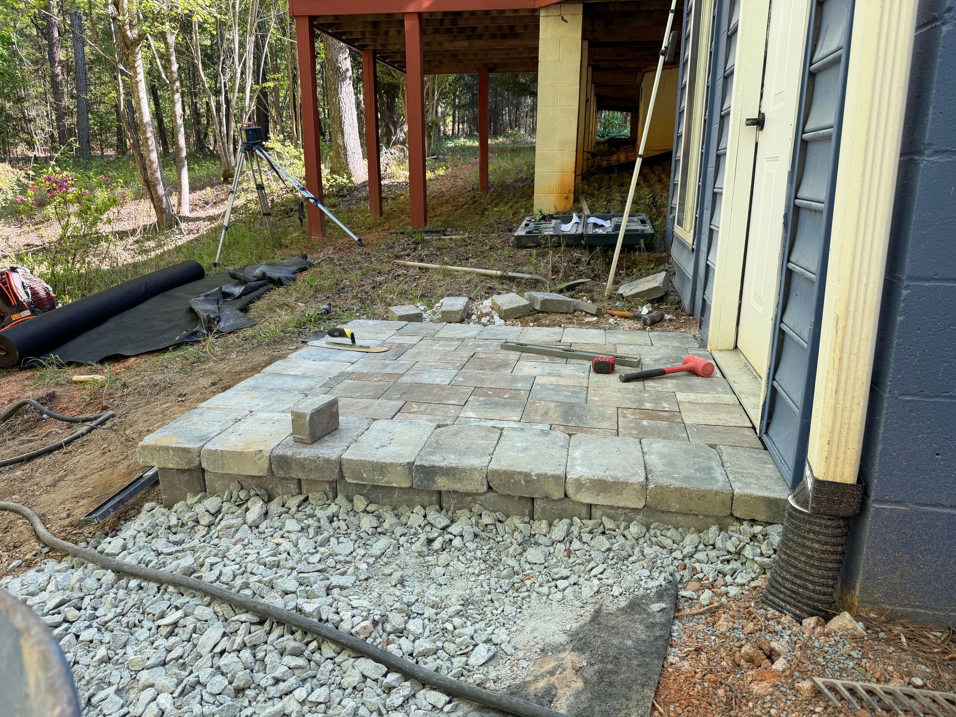 Backyard patio under construction with pavers, gravel, and a covered porch beside a house
