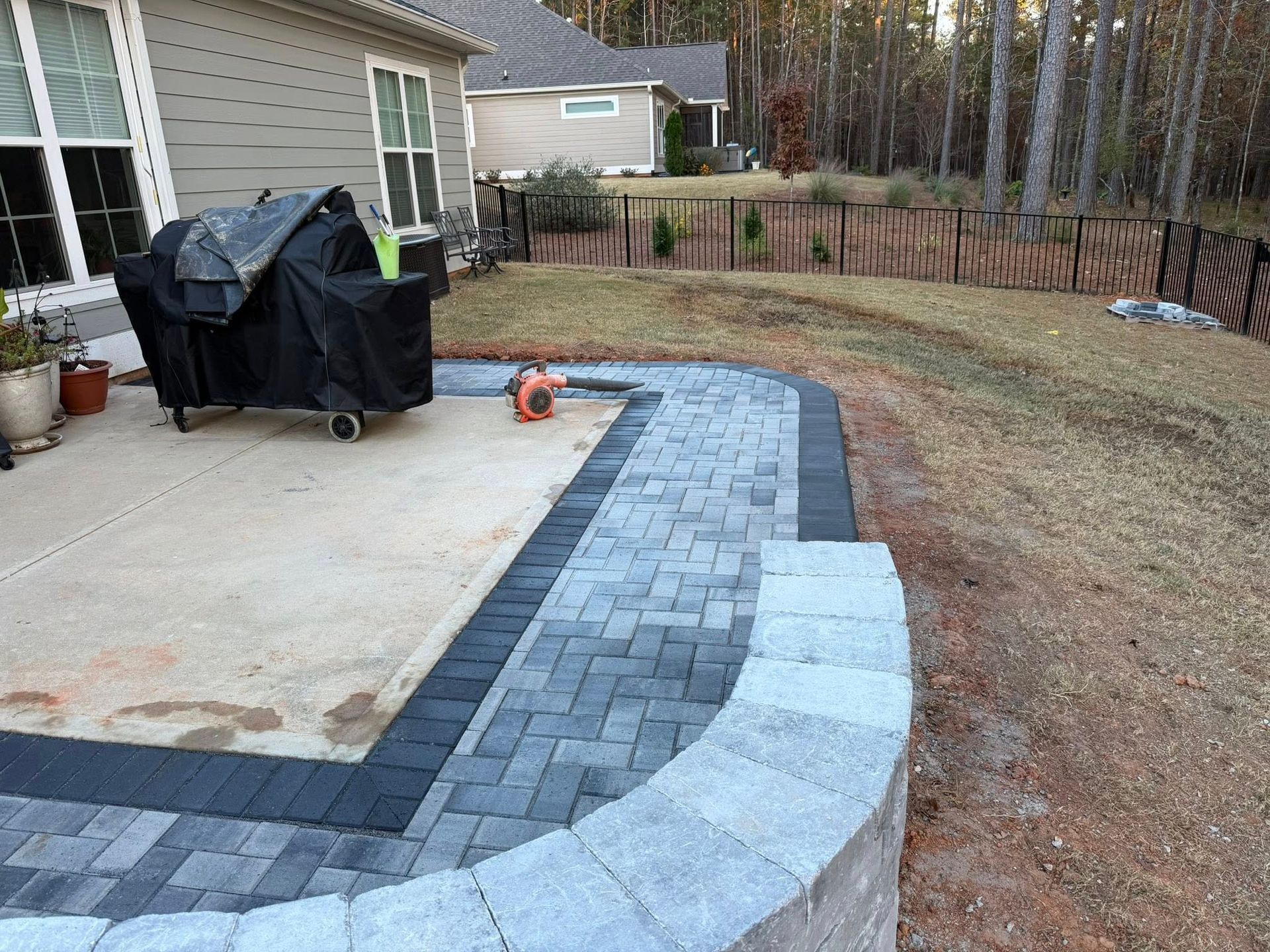 Patio with a curved gray paver border and light concrete edge beside a house and yard
