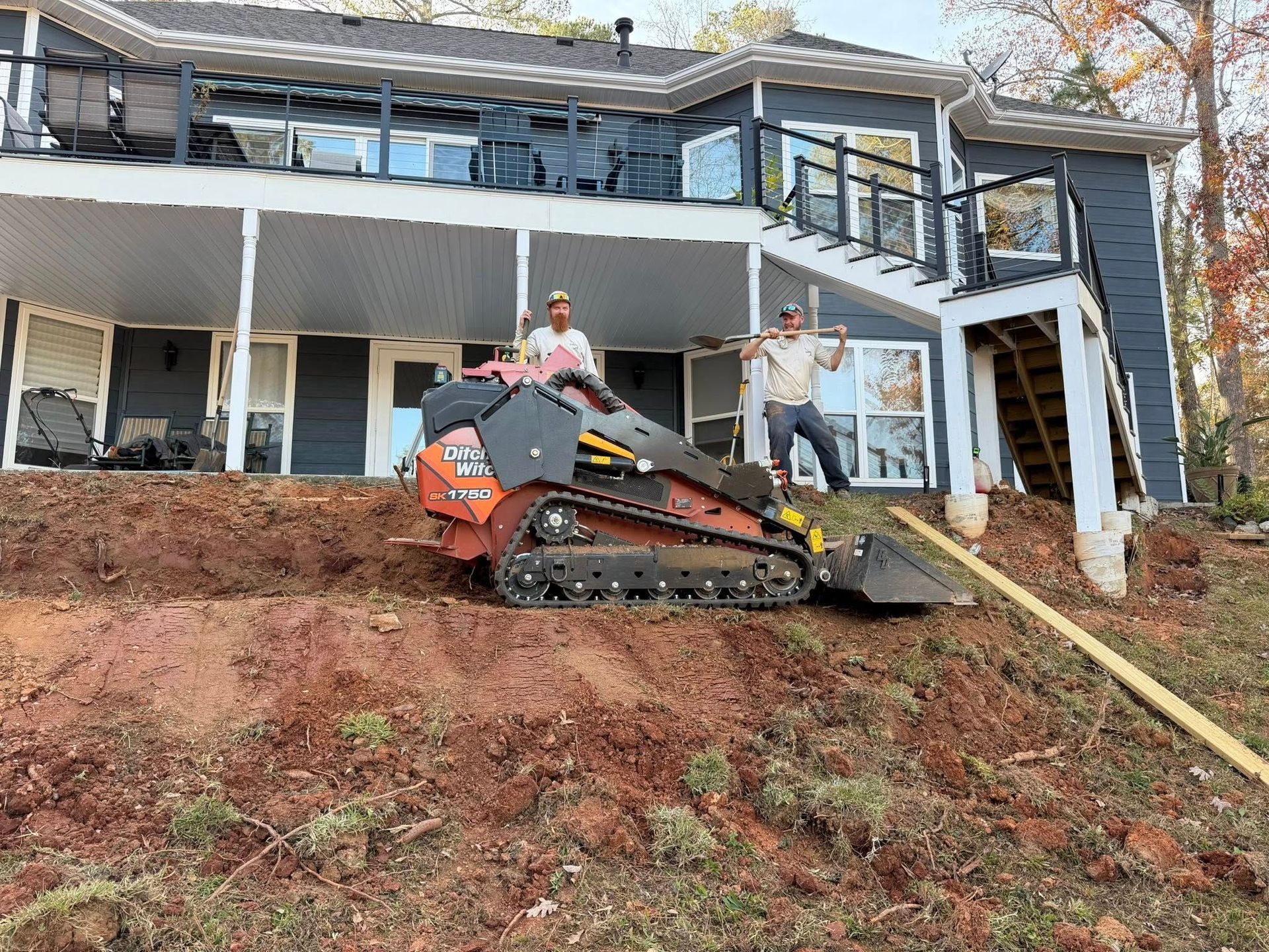 Person on an orange skid-steer clearing debris on a steep hillside by a damaged house