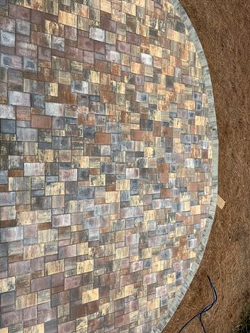 Round mosaic tabletop with multicolored square tiles on a brown floor, with a black cable nearby