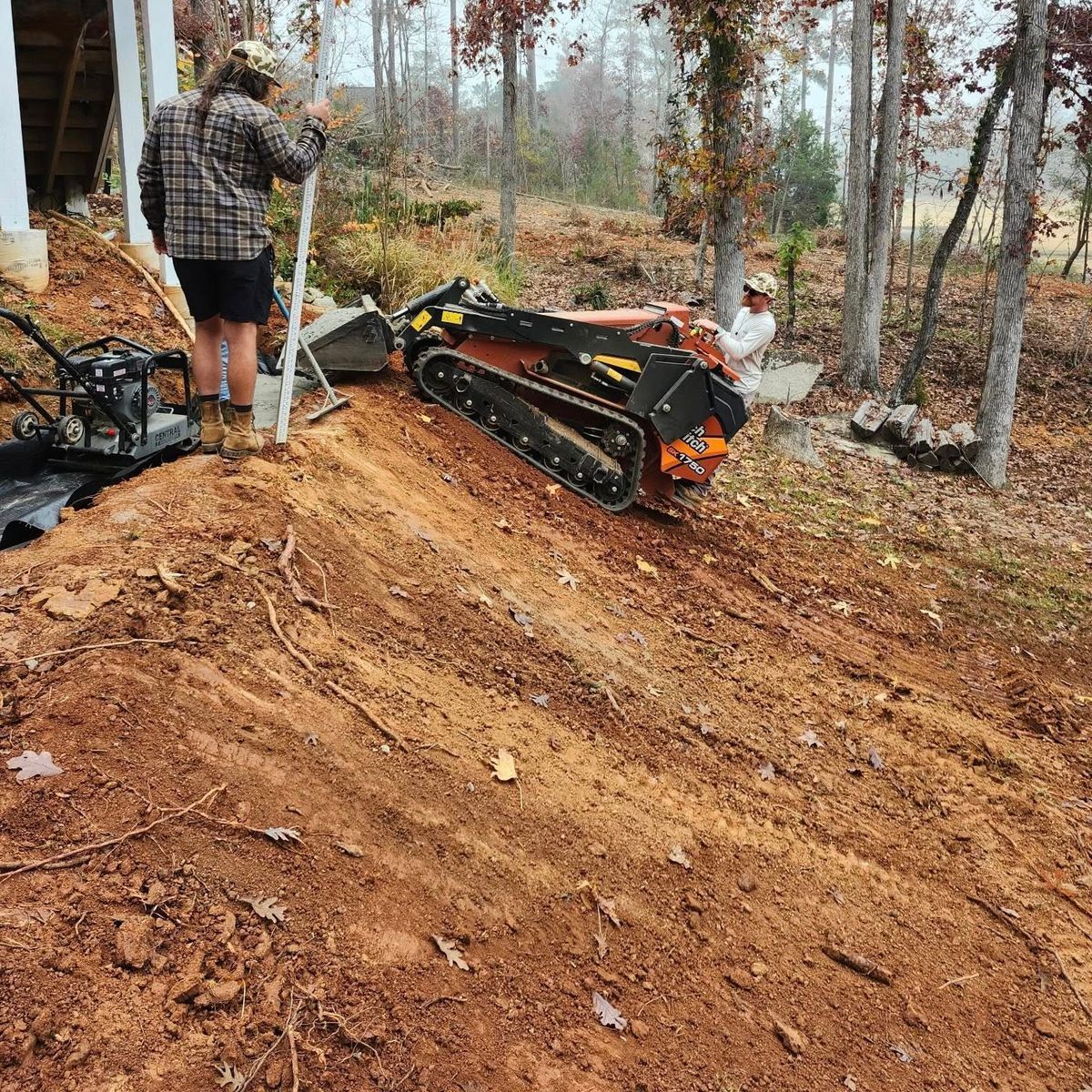 Person beside a tracked machine on a muddy forest slope, with a chain saw nearby.
