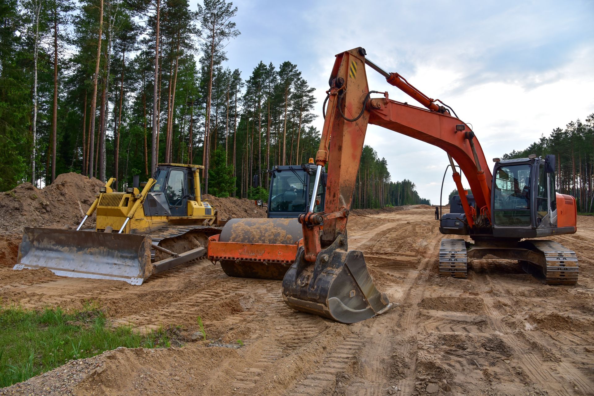 Excavator, bulldozer, and backhoe at a forest construction site on muddy ground