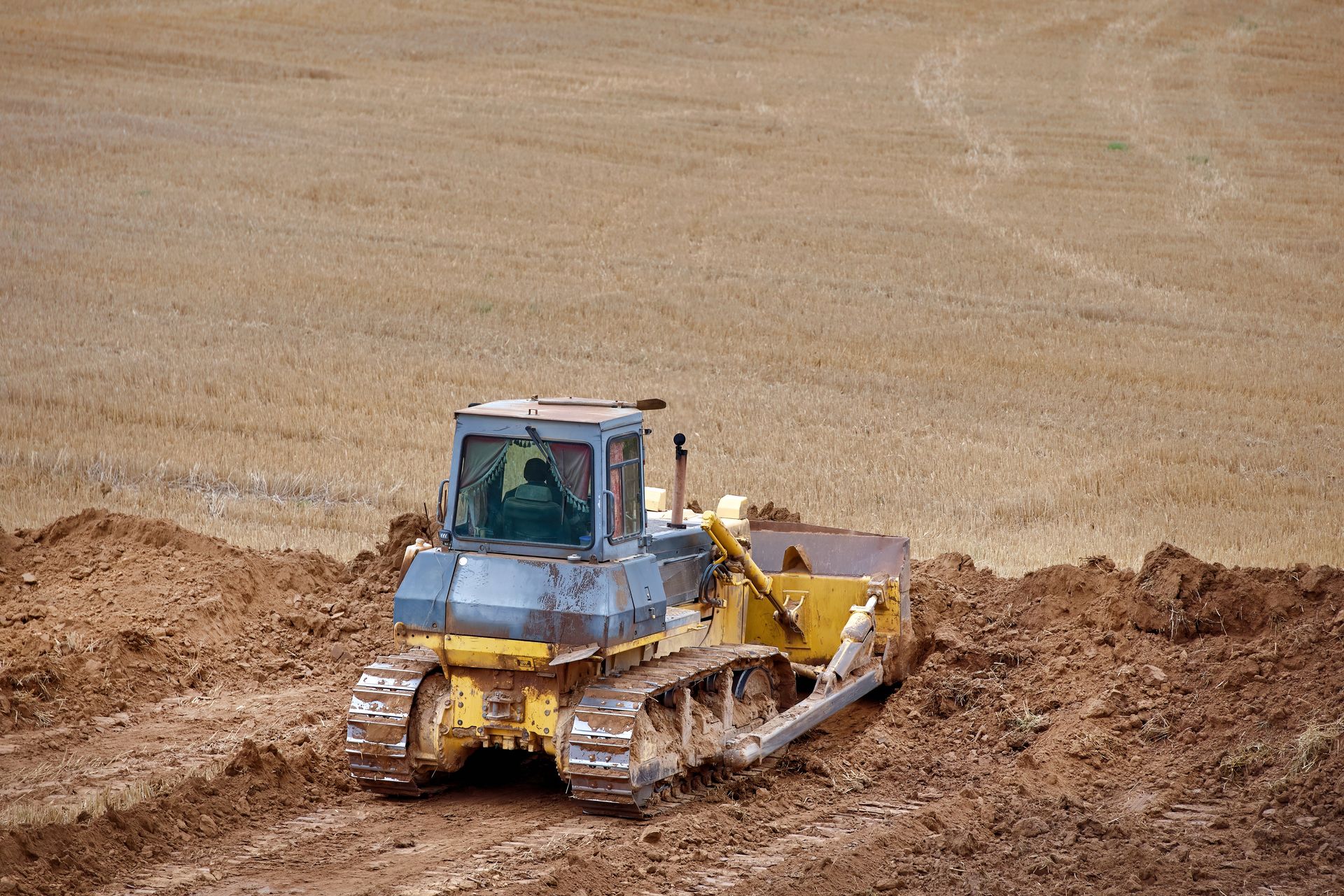 Yellow bulldozer leveling dirt in a brown field under clear daylight