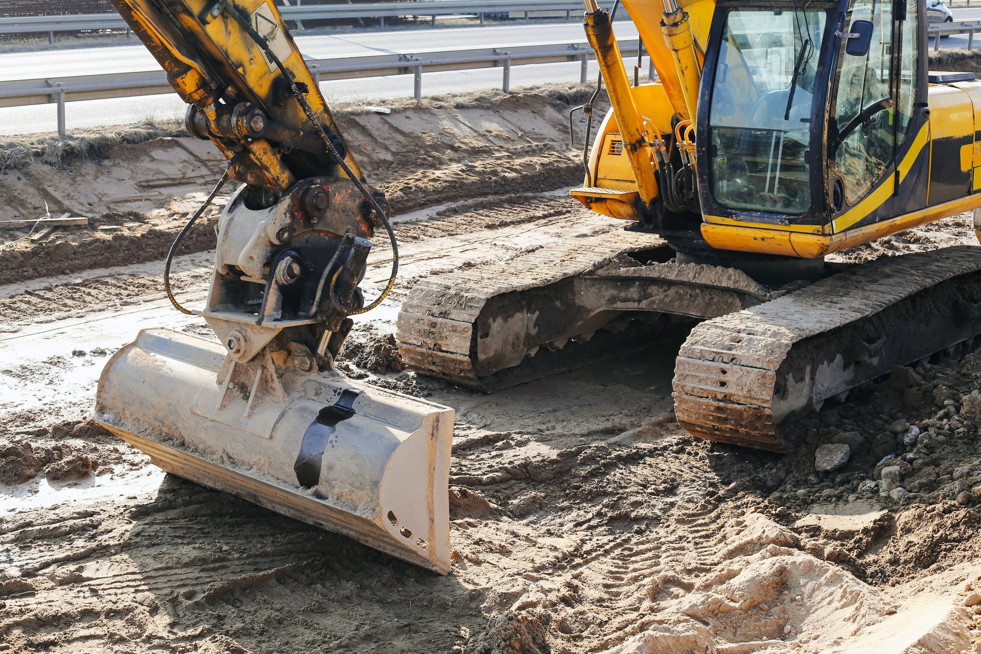 Yellow excavator grading muddy ground at a construction site