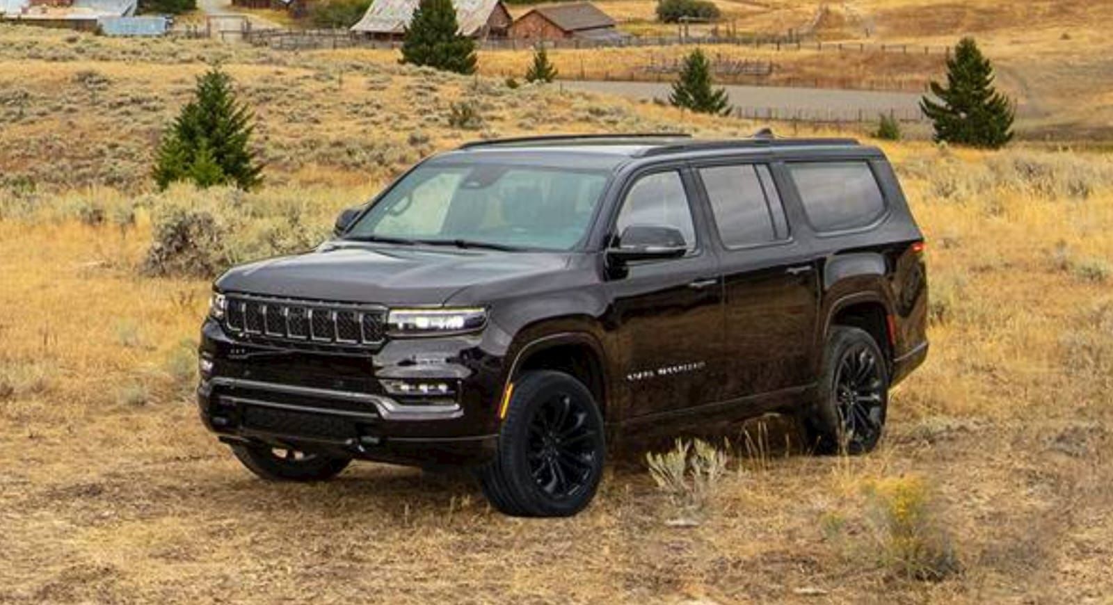 A black jeep grand wagoneer is parked in a dry grassy field.