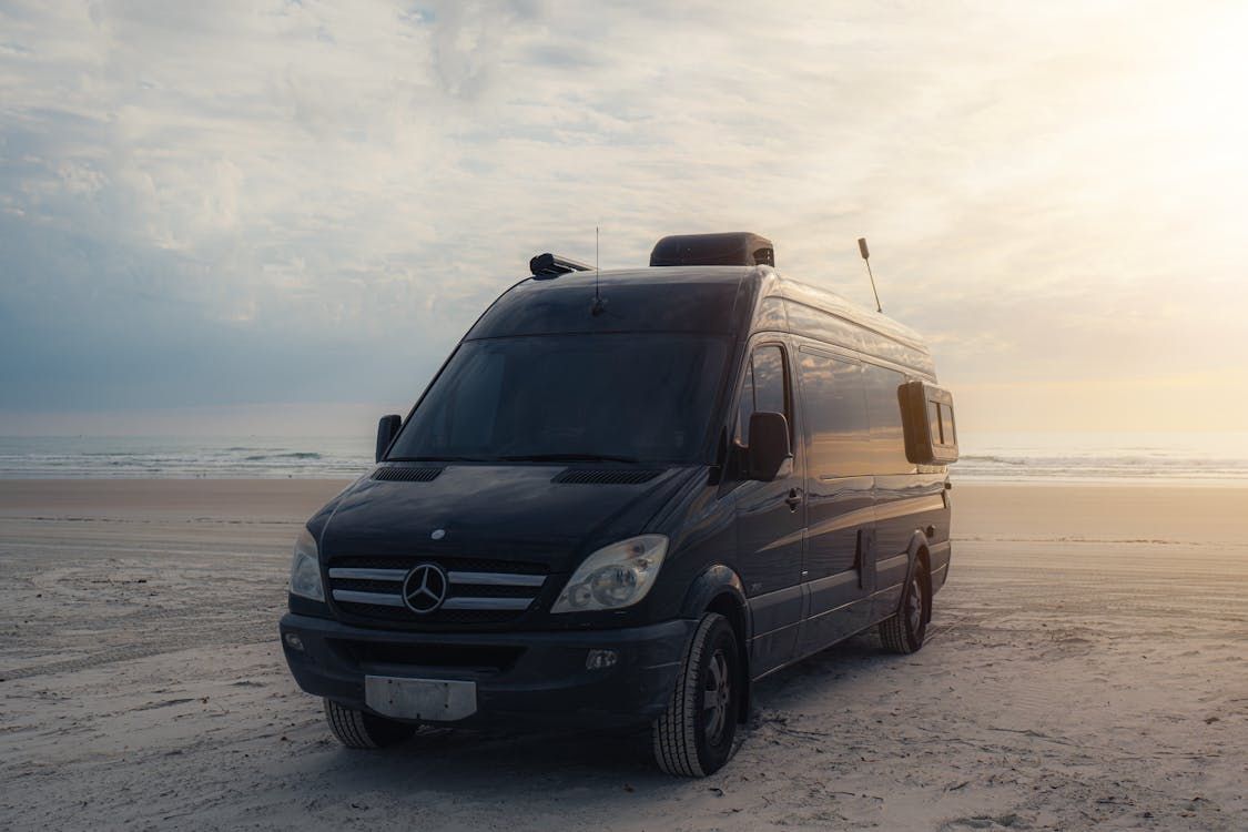 A black van is parked on the beach at sunset.