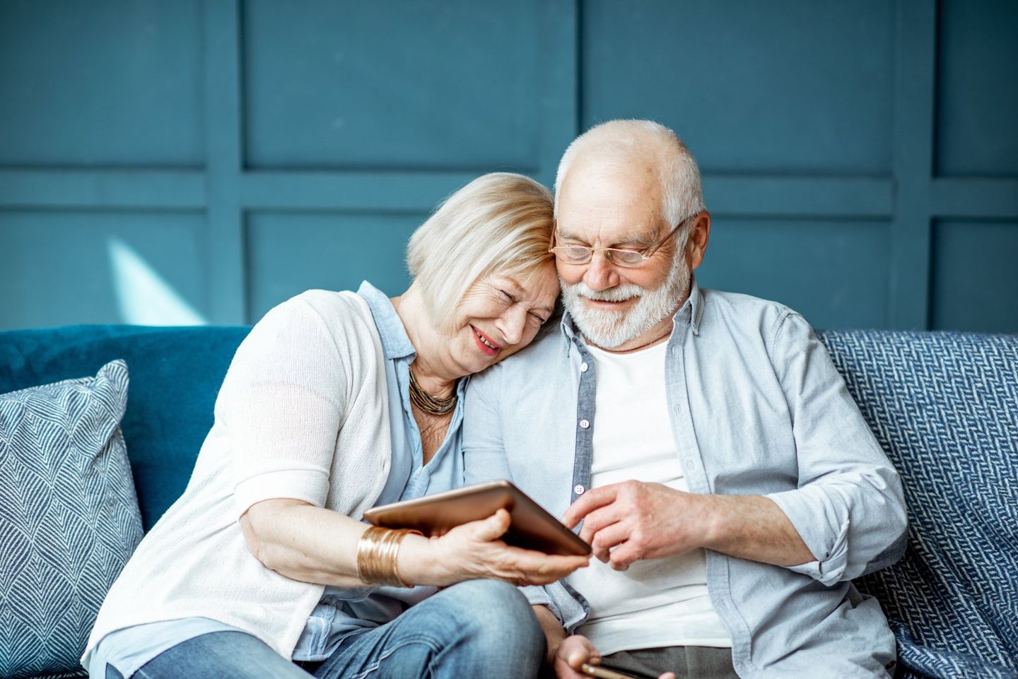 an elderly couple sitting on a couch looking at a tablet