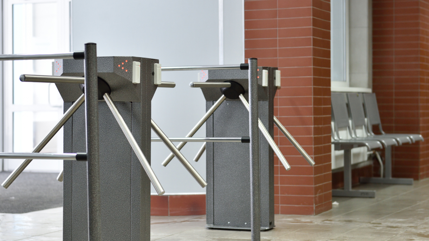 A row of turnstiles are in a hallway next to a brick wall.