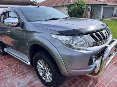 Silver SUV parked in a driveway beside a house, front view with chrome bull bar and side steps