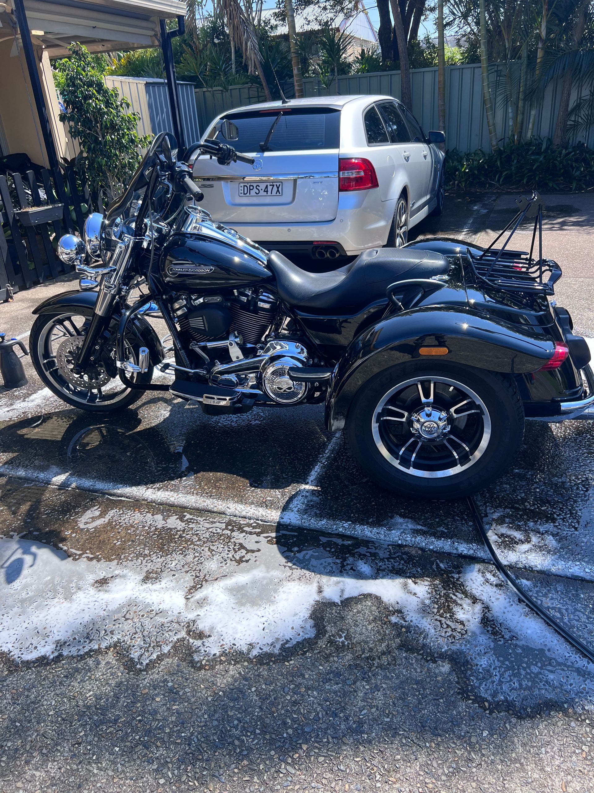 Black Three-wheeled Motorcycle Parked In A Driveway, With A White Pickup Truck Behind It And Wet Pavement Nearby — Car Detailing Mobile Cleaning Co In Port Macquarie, NSW