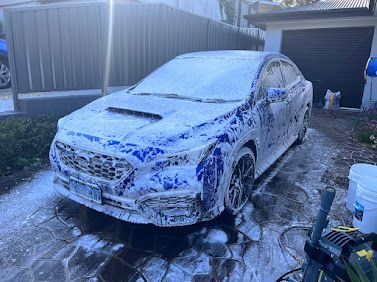 White sedan covered in soap foam in a driveway, being washed outdoors