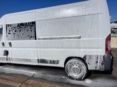 White cargo van with muddy lower panels parked on a sunlit street