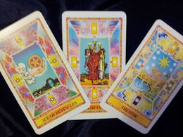 Tarot card spread: Ace of Pentacles, Three of Cups, and The Sun; colorful illustrations on a dark surface.