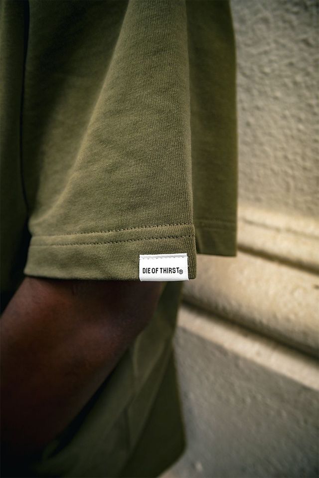 Close-up of olive green t-shirt sleeve with a white label; person's arm visible.
