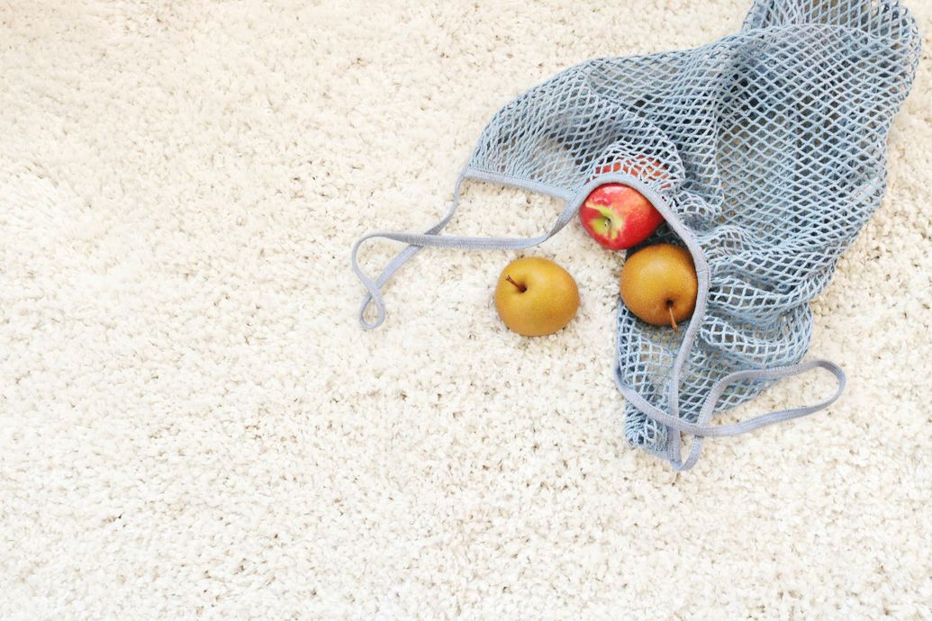 Mesh bag with apple and pears on a white, textured surface.