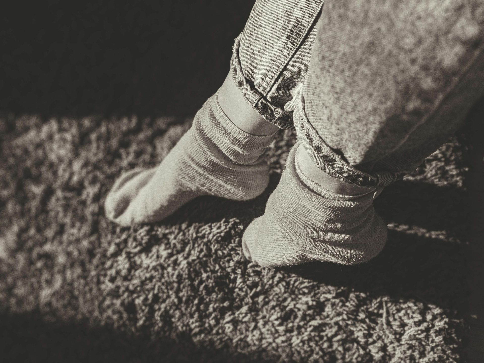 Feet in white socks and jeans on a textured, dark surface.
