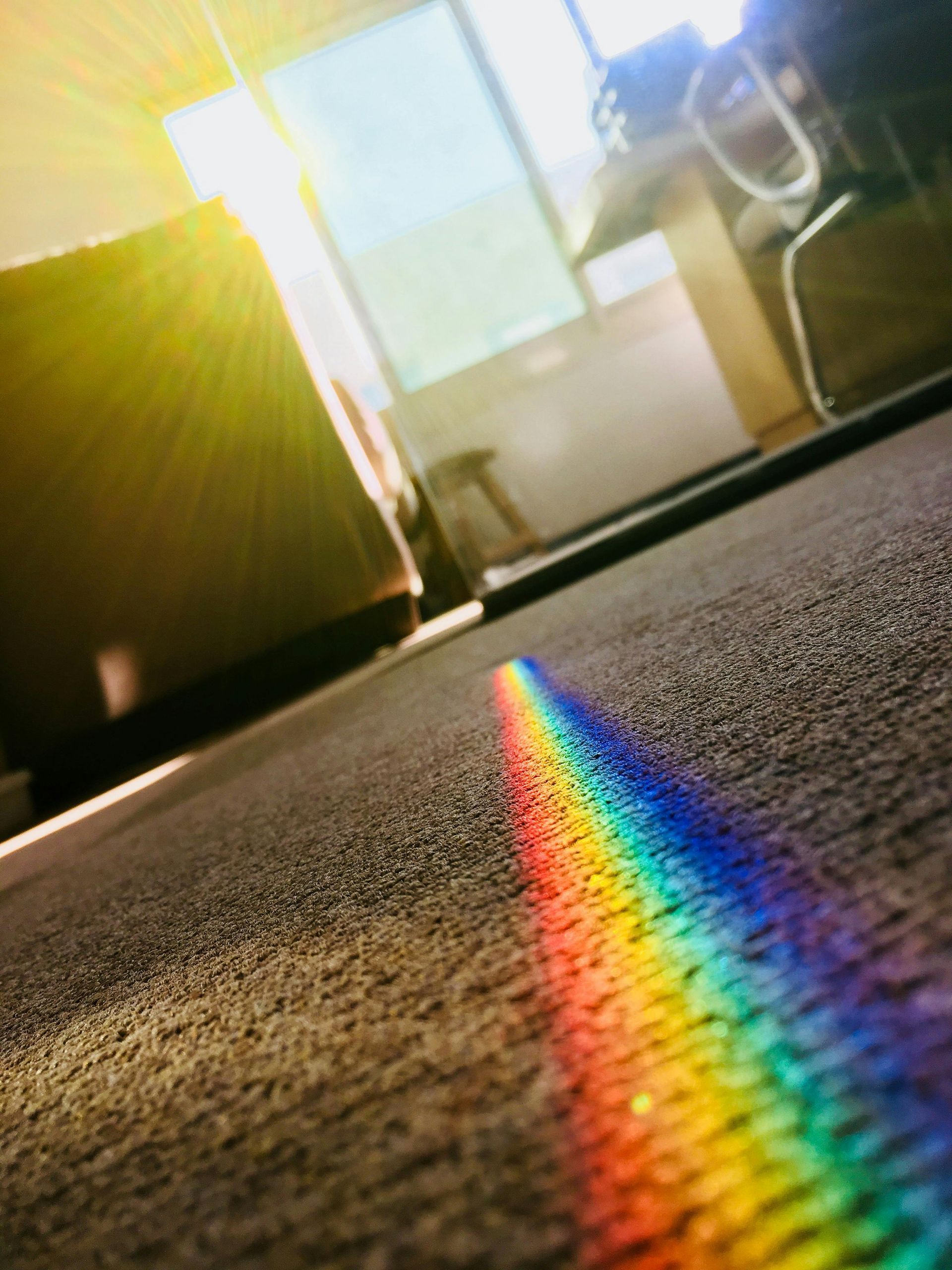 A rainbow spectrum of light on a carpet, bright sunlight streaming through a window.