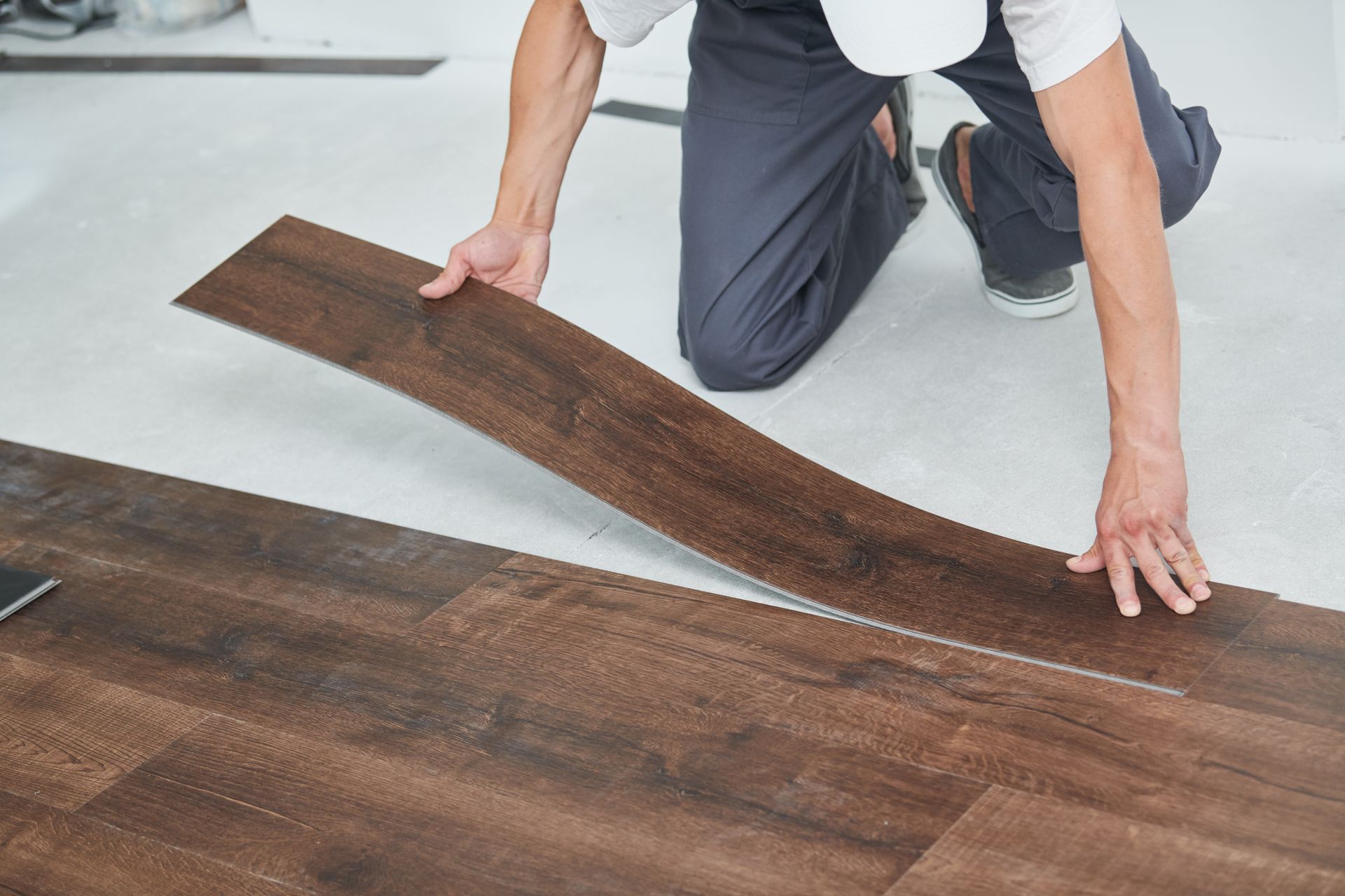 Person installing dark wood-look flooring on a white surface, kneeling and holding a plank.
