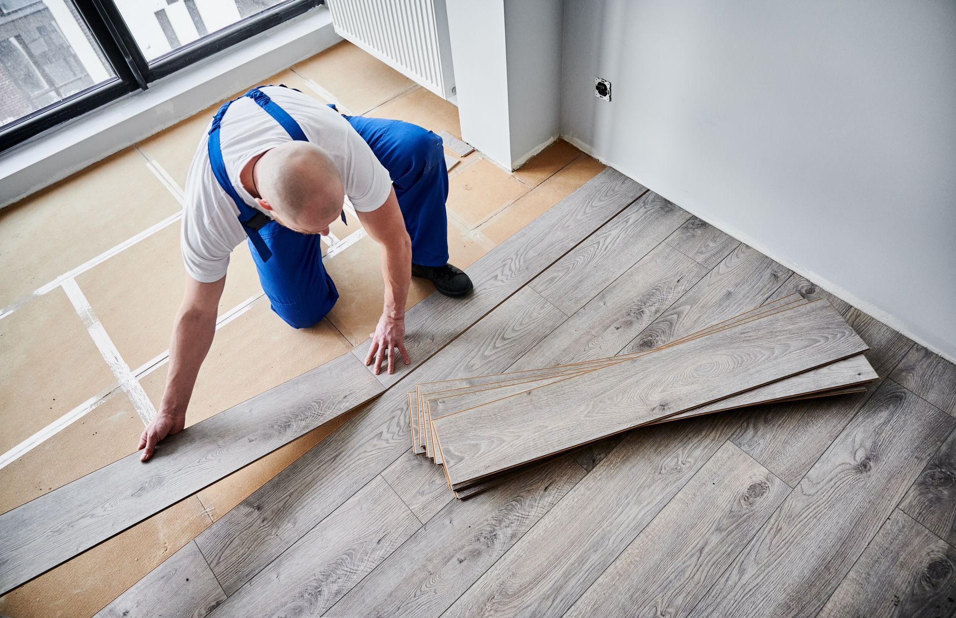 Man installing gray wood flooring in a room.
