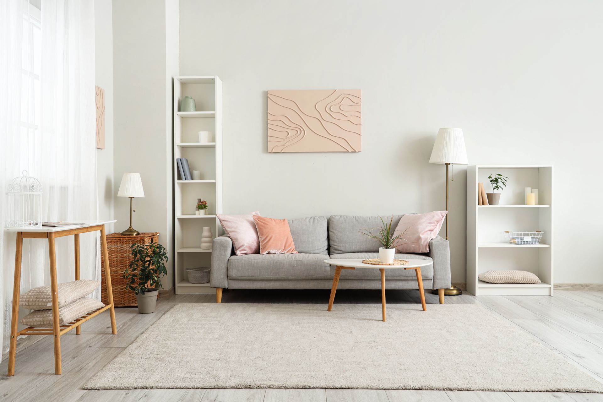 Living room with a gray sofa, light wood furniture, white bookshelves, and a cream rug.