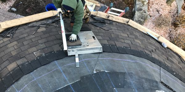 A man from Constantine Roofing in Shelby Township, MI is replacing a shingle on a roof.
